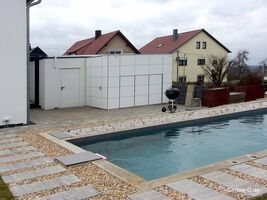 Moderner Garten mit Pool, Steinweg, Grill und Weißem Schuppen, im Hintergrund Häuser.