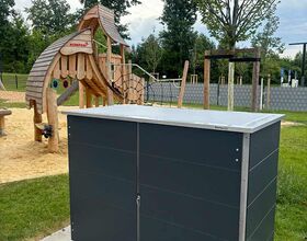 Spielplatz mit Rutsche und Klettergerüst, daneben ein großer grauer Schrank auf einer gepflasterten Fläche.