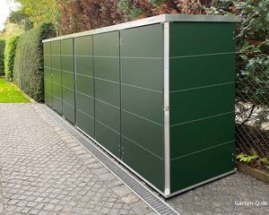 Großer grüner Gartenschrank auf gepflastertem Weg, umgeben von Hecken und Bäumen.