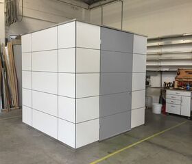 Ein würfelförmiger Raum in einem Arbeitsbereich, umgeben von Werkzeugen und Regalen.