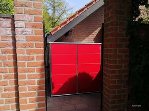 Roter Schrank oder Schuppen in einem Hof, umgeben von Backsteinmauern und Laub.