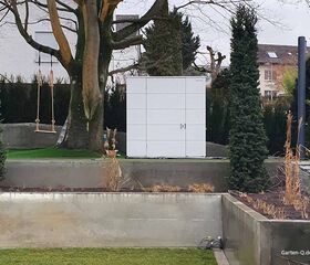 . Ein Garten mit Baum, Schaukel, weißem Schrank und Pflanzen.