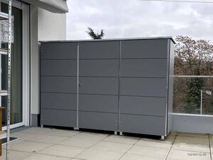 Grauer Metallschrank steht auf einer Terrasse neben einer Leiter und Fensterfront.