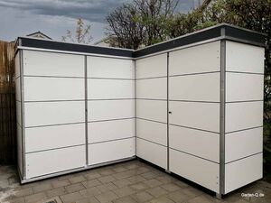 Ein modernes Gartenschuppen aus weißen Paneelen auf Pflastersteinen.