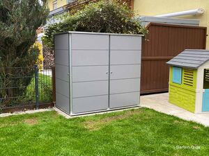 Ein grauer Gartengeräteschrank neben einem Spielhaus in einem kleinen Garten