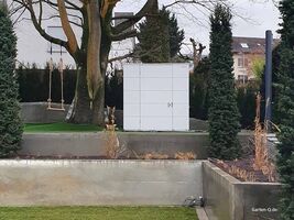 . Ein Garten mit Baum, Schaukel, weißem Schrank und Pflanzen.